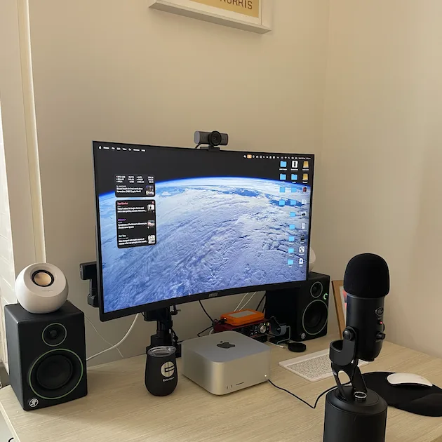 My complete tech setup: a 32-inch curved MSI monitor, Mac Studio, Logitech Brio webcam and Blue Yeti microphone on a desk